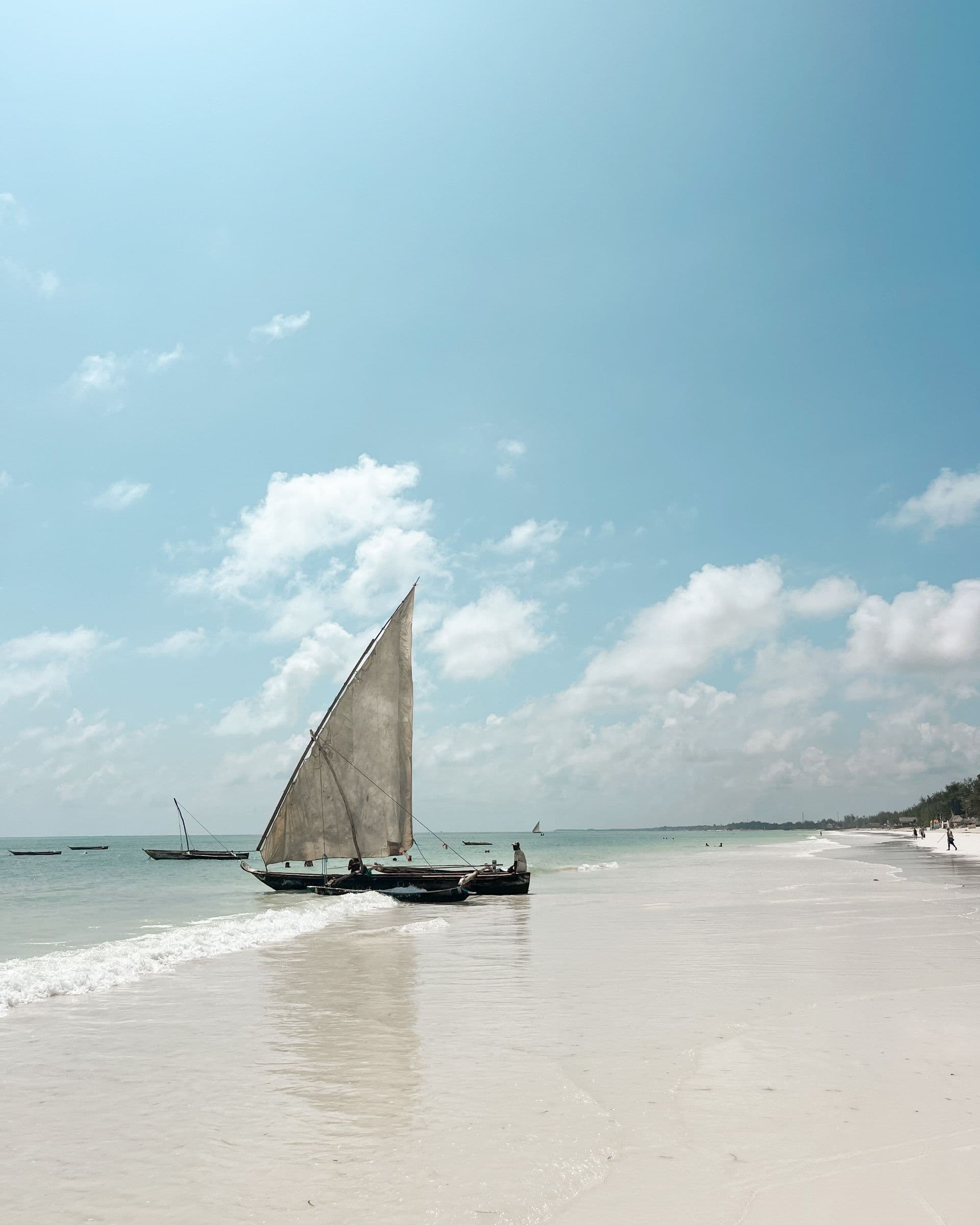 A dhow on white sand beside turquoise water